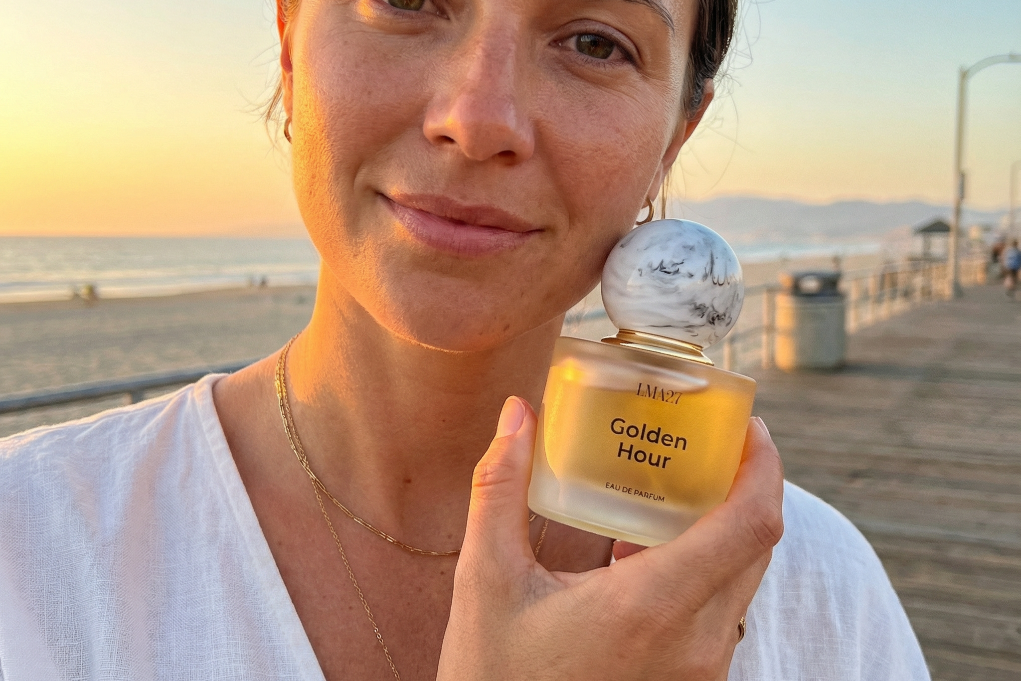 Woman holding LMA27 Golden Hour eau de parfum bottle on the beach during golden hour