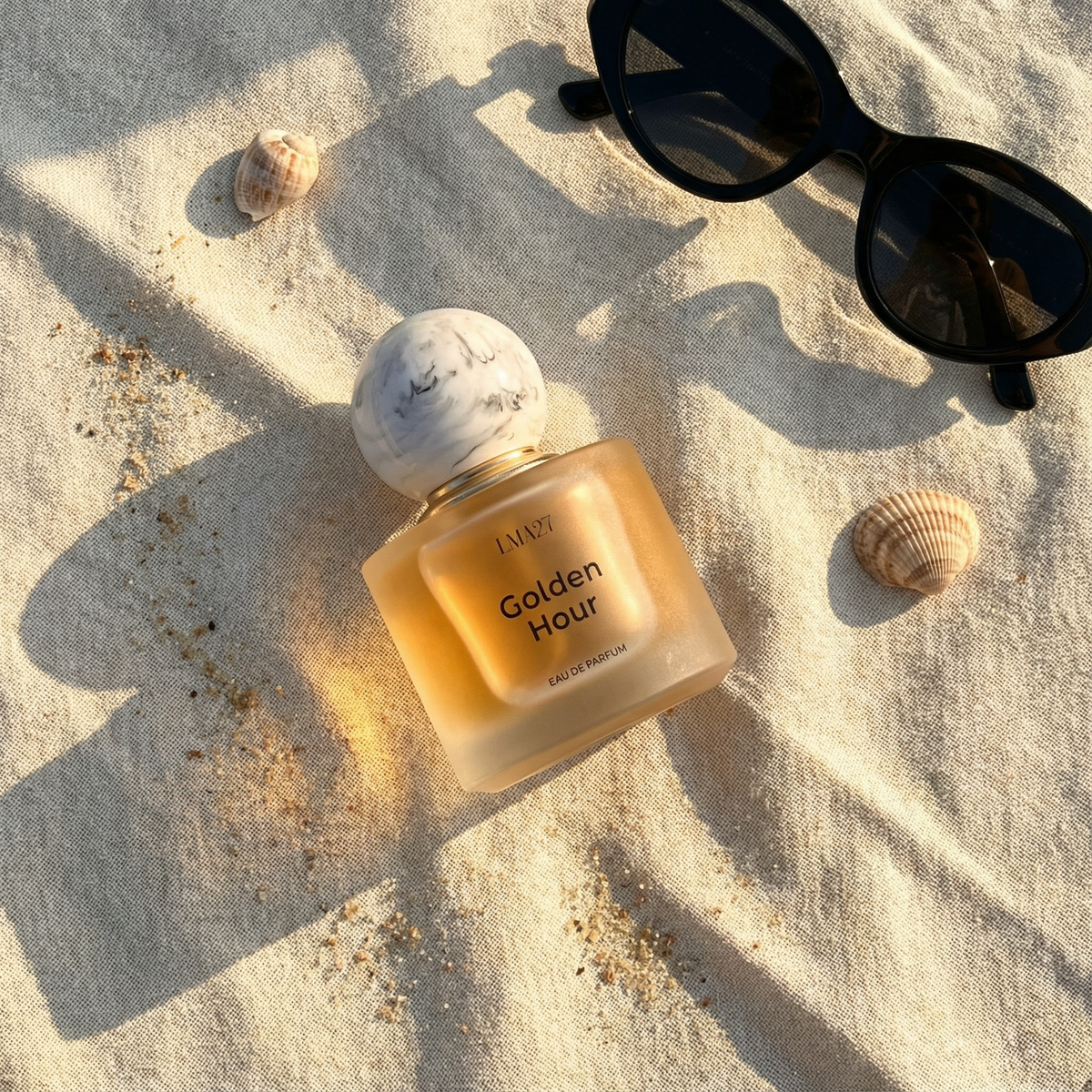 Perfume bottle labeled 'Golden Hour' on sand with sunglasses and shells