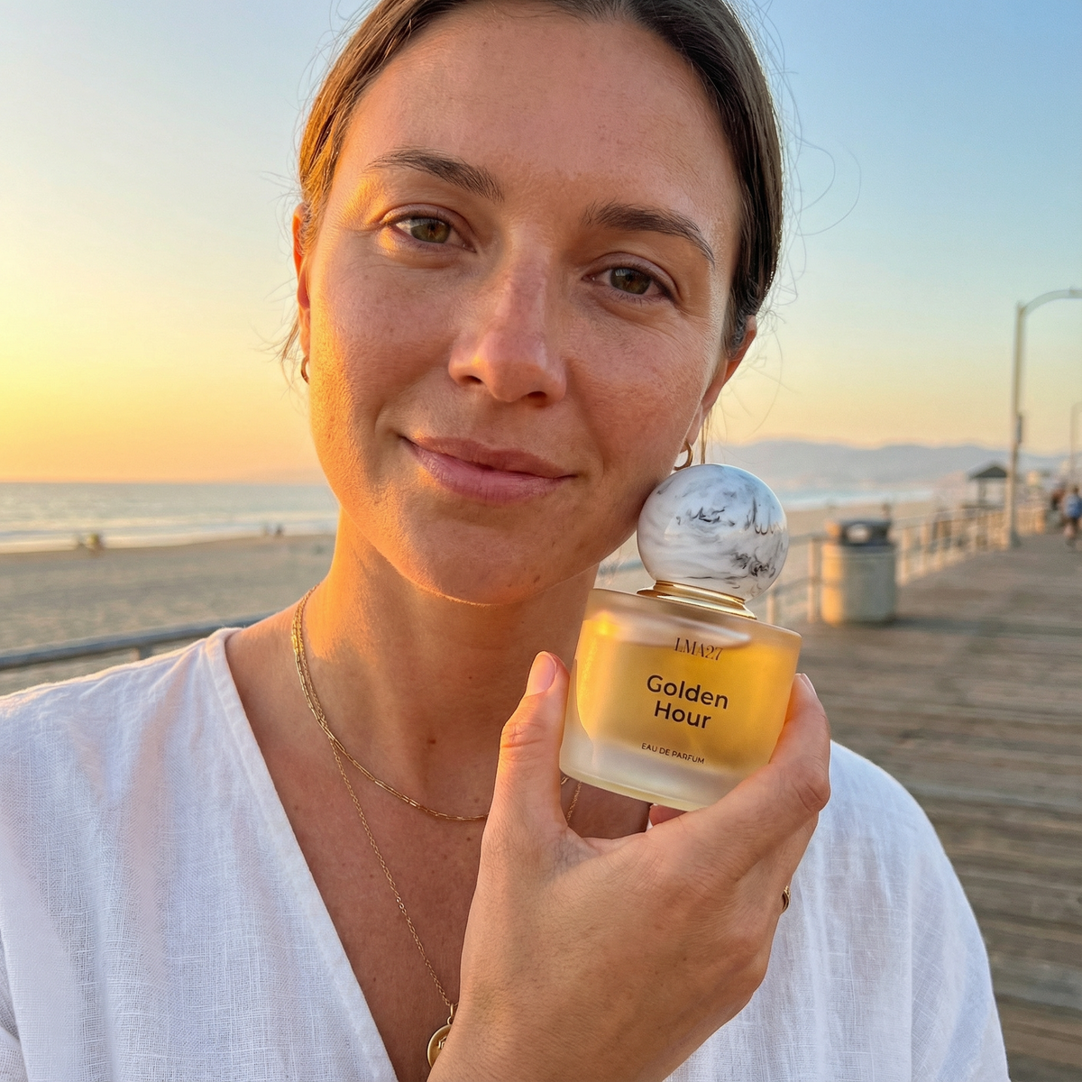 Woman holding a product labeled 'Golden Hour' by the beach at sunset.