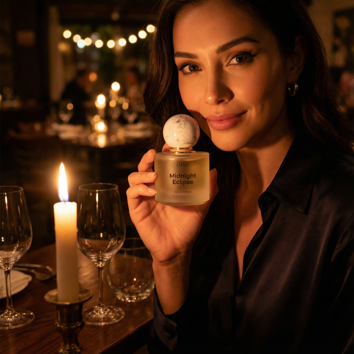 Woman holding LMA27 Midnight Eclipse eau de parfum bottle at a candlelit restaurant table