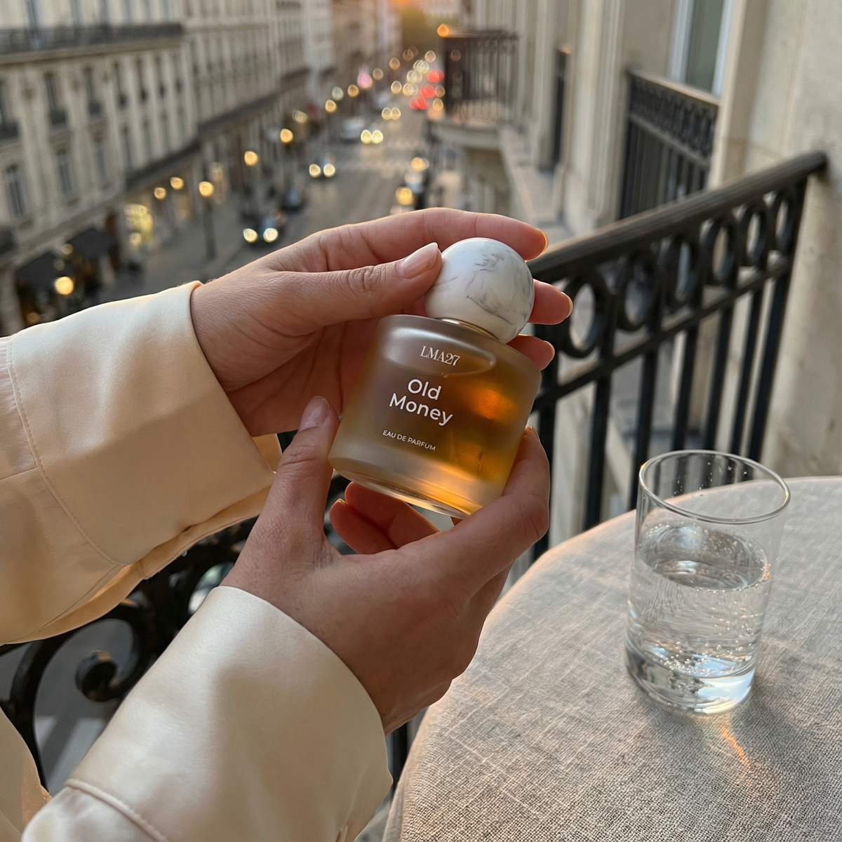 LMA27 Old Money perfume bottle held on a balcony with evening city lights in background