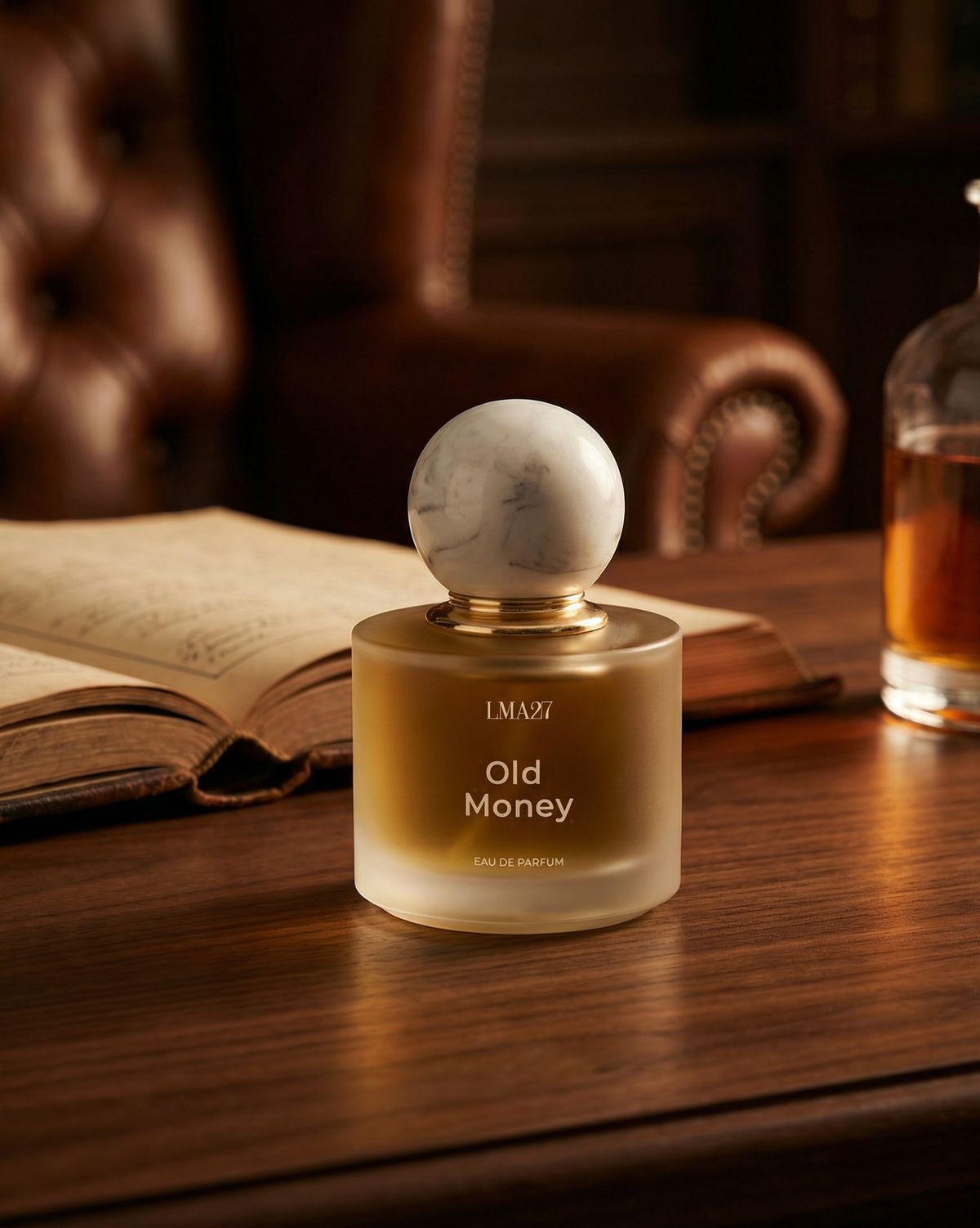 LMA27 Old Money perfume bottle on a wooden desk with books and leather chair in warm light